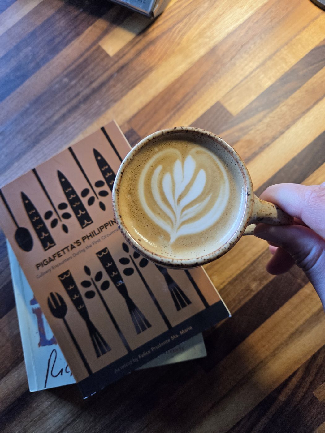 Latte with rosetta latte art held over a wooden table at Bukas Cafe