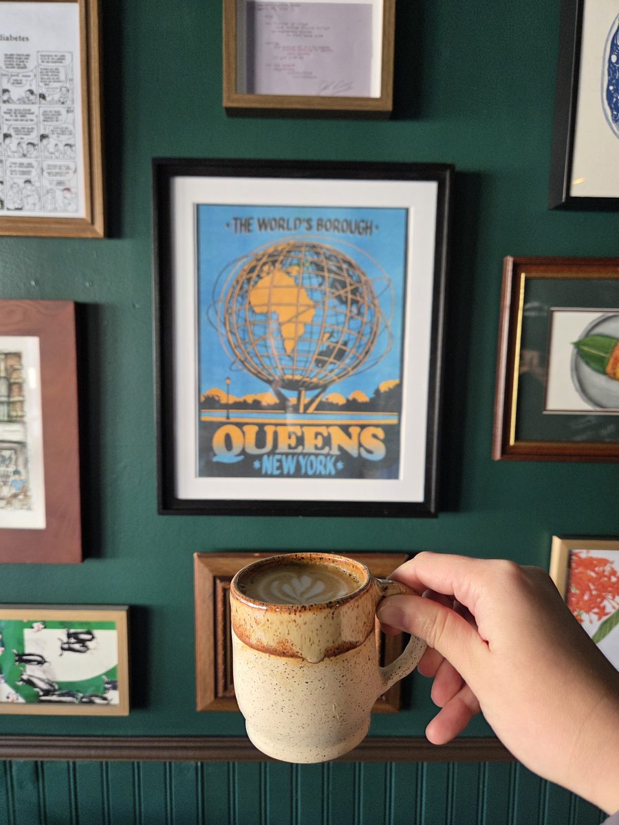 Hand reaching for a ceramic mug beneath a framed Queens poster