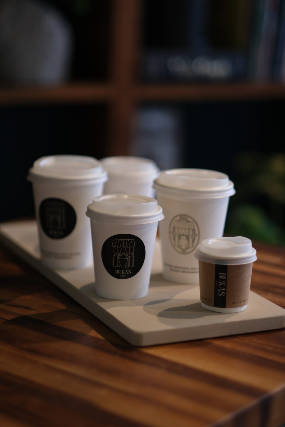 Bukas Cafe branded to-go cups arranged on a tray against a deep green wall